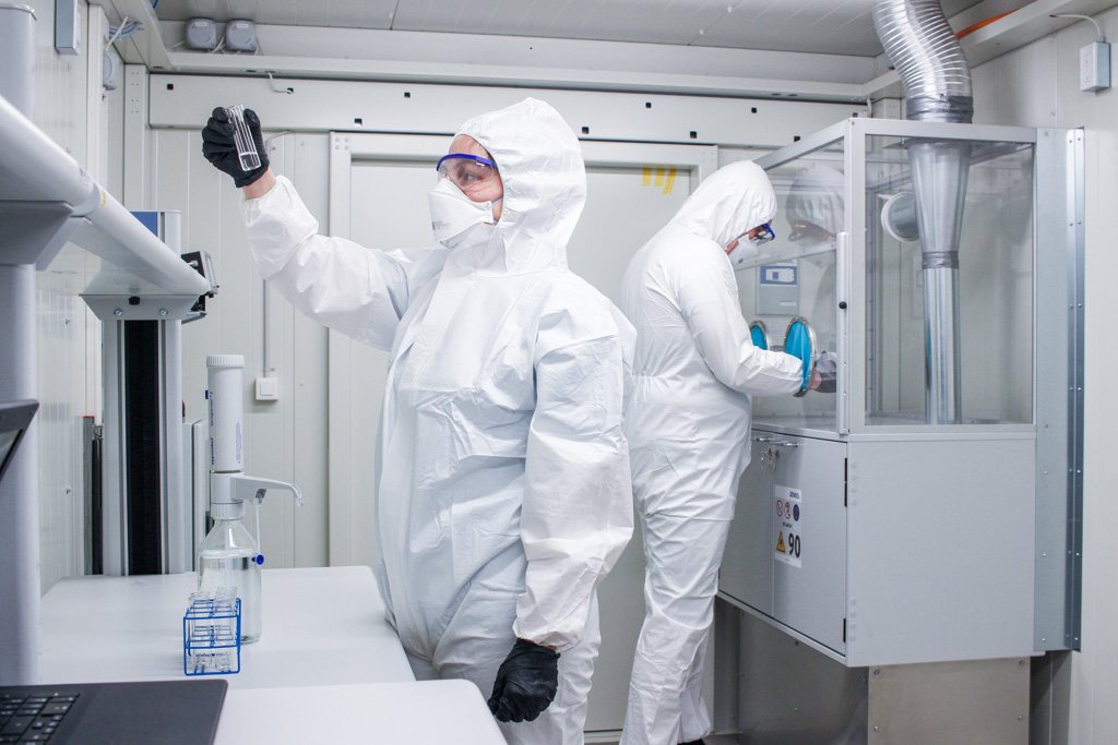 Two operators in protective suits working inside a smolsys container laboratory
